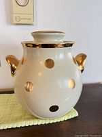 Front view of Hall's ivory ceramic cookie jar with gold polka dots and handles