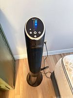 Full view of Honeywell black tower fan next to bed