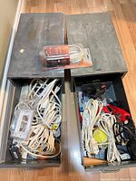 Two metal drawers opened showing extension cords, packaged NOMA cord, hot glue gun, adapters