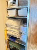 Stacked white linens and assorted plastic storage containers on shelving