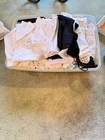 Plastic bin filled with folded white, black and light-colored short-sleeve tops
