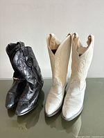 White and black leather cowboy boots side by side on glass surface
