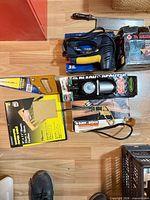 All seven items laid out on floor showing drill box, sander box, jigsaw, inflator, hand saw, sandpaper and other tool