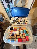 Two clear tubs filled with assorted thread spools, blue lid visible