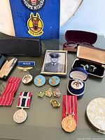 Overview of medals, pins, cufflinks, photograph and compact on table