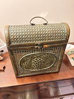 Front view of chest showing grape medallion, woven cane panels, latch