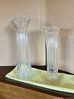Two clear glass ribbed bud vases standing upright on cloth