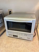 Front and top view of Panasonic NB-G110P toaster oven displaying control panel and glass door