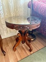 Full view of round wooden pedestal accent table with glass top