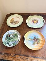 Four assorted decorative wall plates on wooden surface