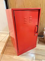 Front view of red metal cabinet showing single door, handle and lock