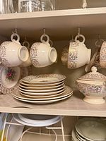 shelf view showing teacups, saucers stack, covered sugar bowl