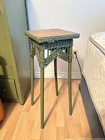 Full view of green wicker stand beside bed