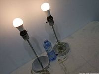 two metal table lamps on table with water bottle for scale