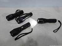 Four black LED flashlights, one illuminated
