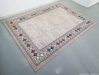 Full view of rectangular beige rug with geometric multicolour border