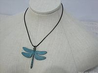 Full view of dragonfly bronze pendant with blue patina on black cord displayed on mannequin bust