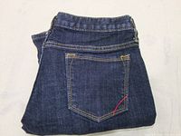Folded dark denim jeans showing back pocket stitching and fabric condition