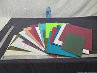 Fanned array of multicolored mat board pieces on table with ruler and bottle for scale