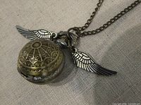 Closed brass-tone Golden Snitch pendant watch showing wings and chain