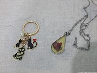 Keychain and pendant necklace laid flat showing charms, pearl, resin rose and chains