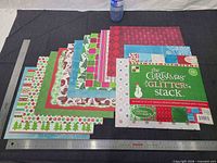 Stacked view of DCWV paper pad with nine loose 12x12 Christmas cardstock sheets; rulers show 12x12 size reference