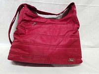 Front view of red Lug shoulder bag showing zip pocket, quilting, logo badge and strap