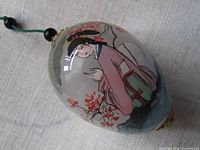 Full view of reverse-painted glass egg ornament showing geisha artwork