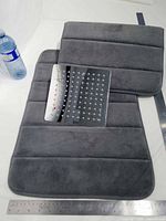 Two grey bath mats and square chrome shower head laid out for full view