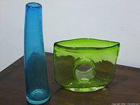 Blue cylindrical vase and green rectangular sculptural vase side by side