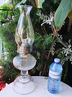 Full view of clear glass hurricane oil lamp beside water bottle for scale