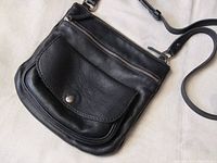 Full view of black leather Roots crossbody showing front flap pocket and strap
