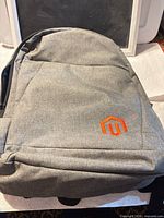 Front view of grey canvas Magento backpack displaying orange logo