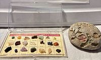 Open acrylic case displaying 21 labeled gemstone specimens next to Serenity stone