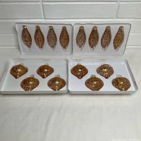 Four plastic trays containing 16 gold glass ornaments in two shapes