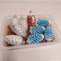 Tray containing nine glass pinecone ornaments in silver, blue/white, red/white colorways