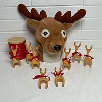Plush reindeer puppet, eight wooden reindeer figurines, red tin with lid displayed against white brick