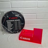 Canon sign in packaging and red acrylic display stand side by side