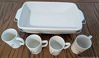 Casserole dish stacked with metal holder and four mugs front view