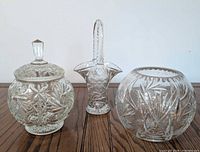Three clear cut crystal pieces: lidded jar, basket vase, round bowl