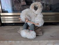 Front view of fur-clad figurine seated on rock, showing pole, knitted pants and fur boots