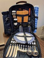 Backpack open showing utensils, plates, glasses, shakers, cutting board