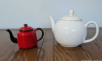 Red metal teapot beside white ceramic teapot showing size comparison