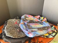 Three backpacks stacked showing Air Jordan elephant print, Stranger Things galaxy print, and Pink Dolphin multicolour camo