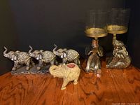 Full lot showing two brass candleholders with hurricanes, triple elephant figurine, soapstone burner