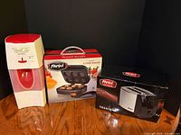 Group shot of three appliances: Mr. Coffee iced tea maker, Parini slider maker box, Parini toaster box