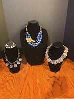 Three statement necklaces displayed on busts