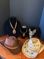 Group shot showing two amber necklaces, bib necklace, brown felt hat, straw hat