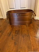 Front view of copper oval planter showing badge and one rope handle