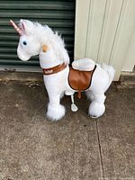 Left side view of white plush PonyCycle unicorn showing saddle, stirrup and wheels